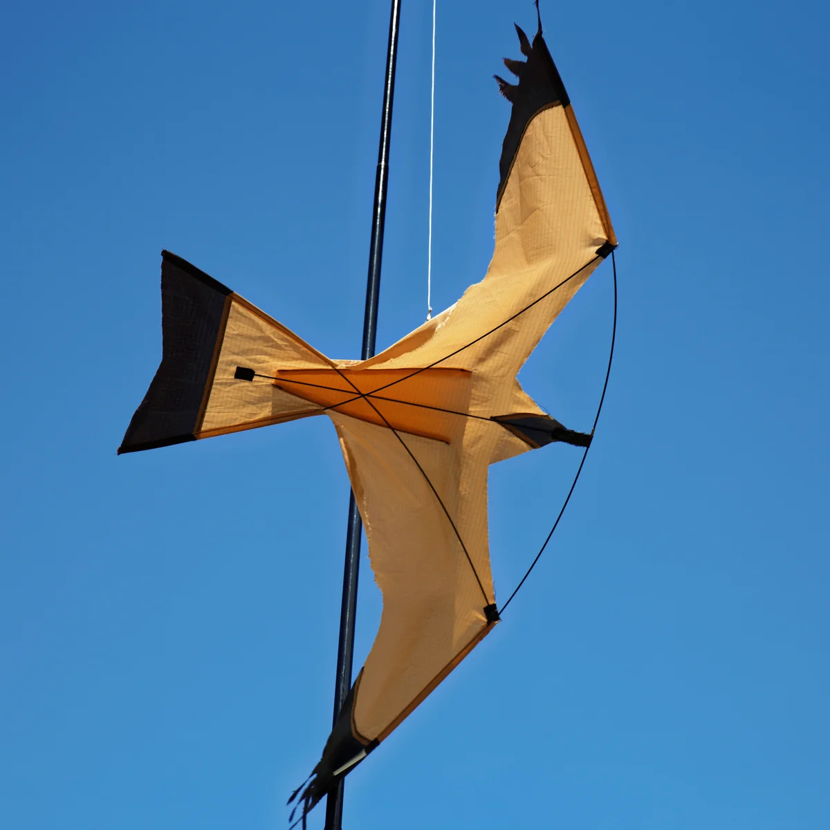 A hawk-shaped bird deterrent kite on a pole against a blue sky